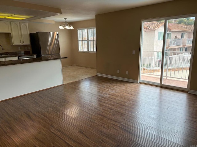 unfurnished living room with baseboards, wood finished floors, an inviting chandelier, and a sink