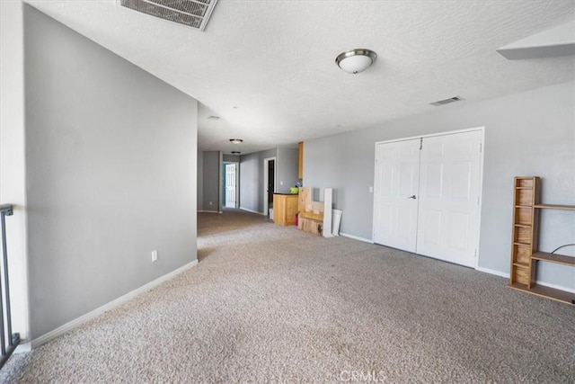 unfurnished living room with baseboards, visible vents, carpet floors, and a textured ceiling