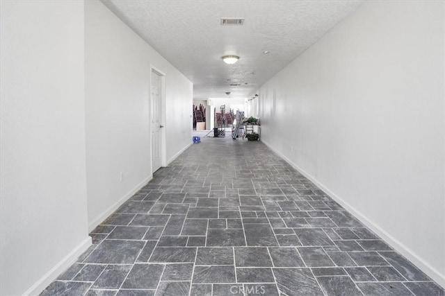 corridor featuring baseboards, visible vents, and a textured ceiling