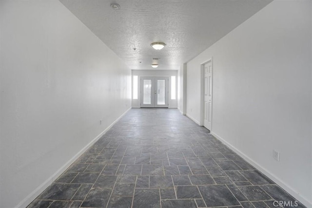 hall featuring baseboards, a textured ceiling, and stone finish floor