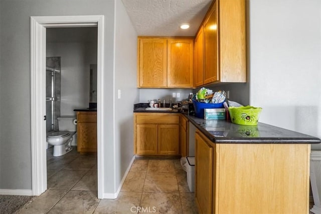 kitchen featuring a peninsula, brown cabinetry, baseboards, a textured ceiling, and light tile patterned flooring