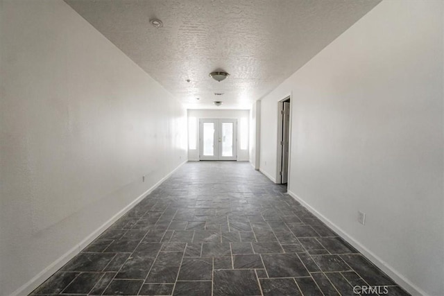 hallway with baseboards, stone finish flooring, a textured ceiling, and french doors