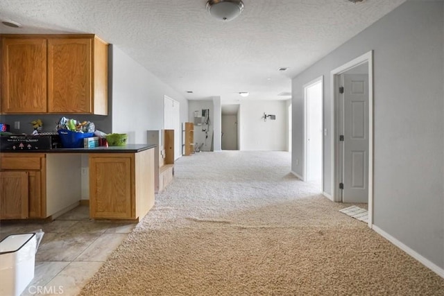 kitchen with baseboards, light carpet, a textured ceiling, and brown cabinets