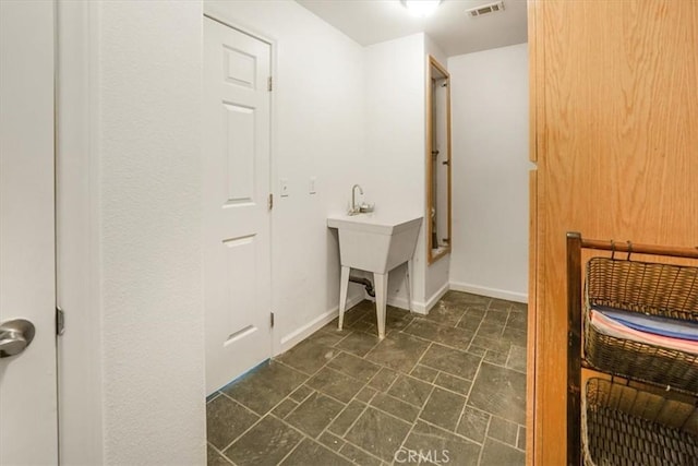 clothes washing area featuring visible vents, stone finish floor, and baseboards
