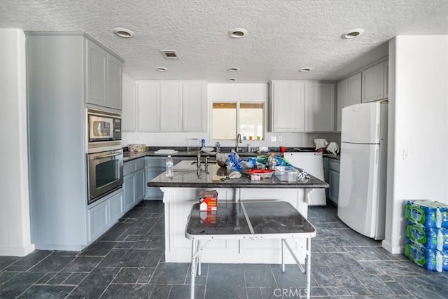 kitchen with stainless steel appliances, a breakfast bar, dark countertops, a textured ceiling, and an island with sink