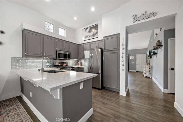 kitchen with gray cabinets, stainless steel appliances, light countertops, a sink, and a peninsula