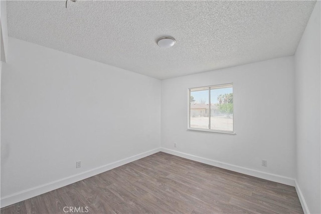 empty room featuring wood finished floors, a textured ceiling, and baseboards