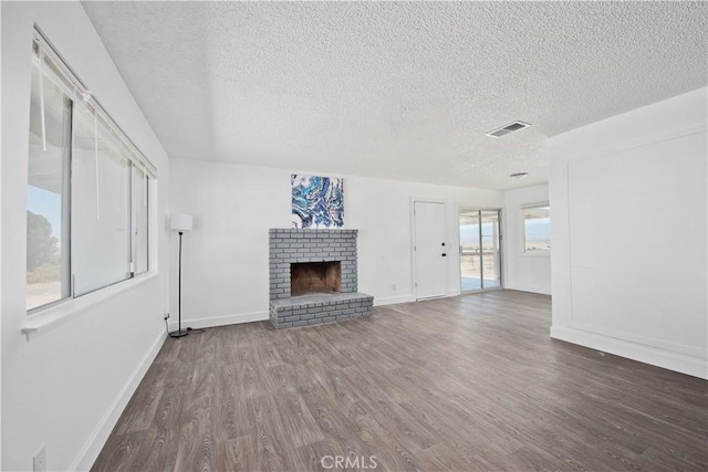 unfurnished living room with wood finished floors, a textured ceiling, a brick fireplace, and baseboards