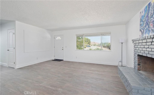 unfurnished living room with a textured ceiling, a brick fireplace, wood finished floors, and baseboards