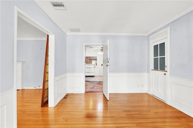 spare room with visible vents, light wood-type flooring, crown molding, and wainscoting