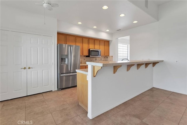 kitchen with stainless steel appliances, a kitchen bar, recessed lighting, a peninsula, and a ceiling fan