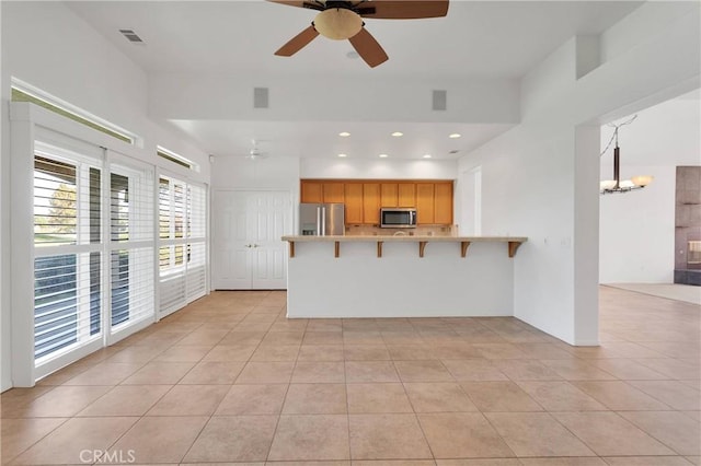 kitchen with a breakfast bar area, stainless steel appliances, ceiling fan with notable chandelier, and a peninsula
