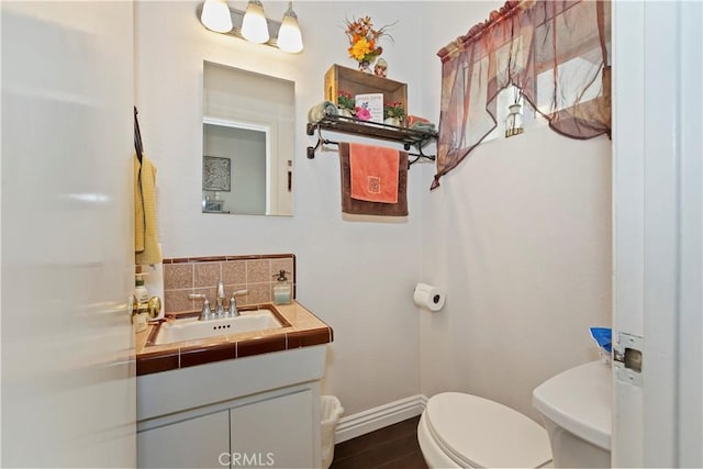 half bathroom with vanity, tasteful backsplash, toilet, baseboards, and wood finished floors