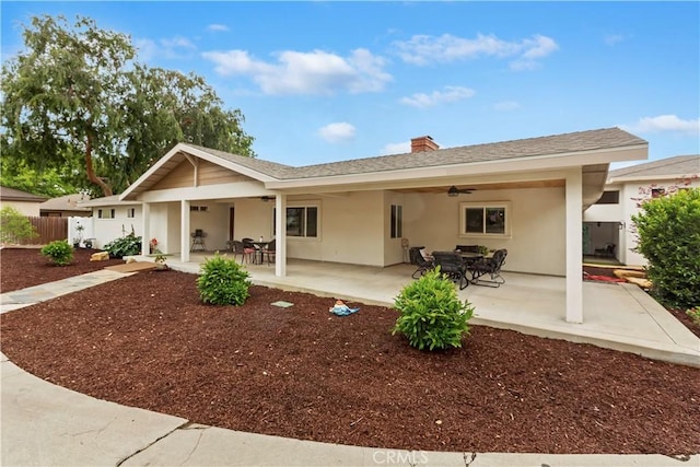 back of house with fence, a chimney, a shingled roof, stucco siding, and a ceiling fan