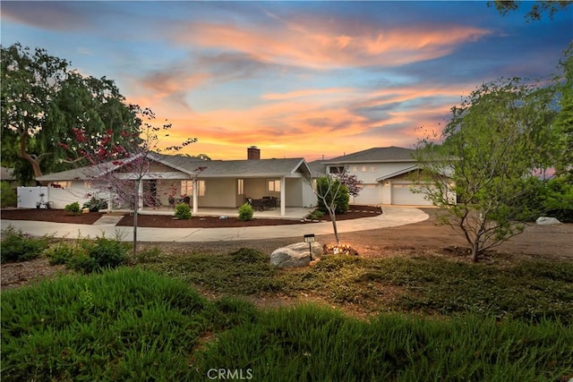 single story home featuring covered porch, stucco siding, curved driveway, and a chimney