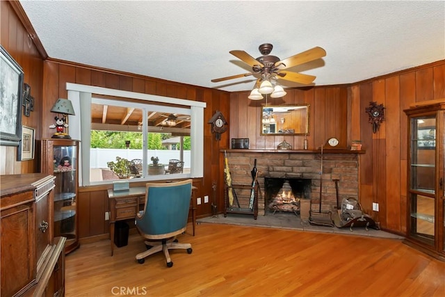 office with a stone fireplace, ceiling fan, wood walls, and light wood-type flooring