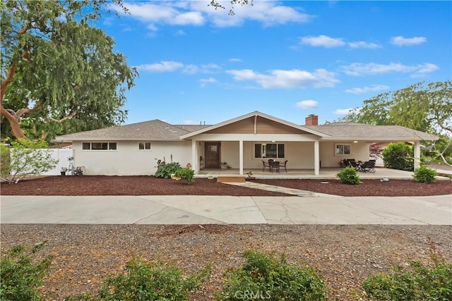 ranch-style home featuring a chimney, a porch, stucco siding, fence, and curved driveway