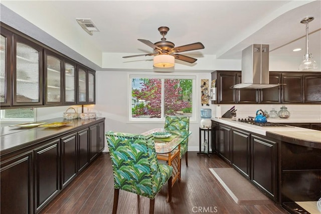 kitchen featuring glass insert cabinets, island range hood, visible vents, stainless steel gas stovetop, and dark brown cabinetry