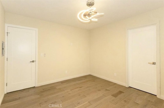 unfurnished room featuring an inviting chandelier, light wood-type flooring, and baseboards