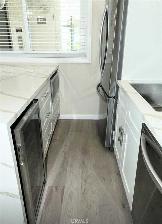 kitchen with beverage cooler, wood finished floors, appliances with stainless steel finishes, white cabinets, and baseboards