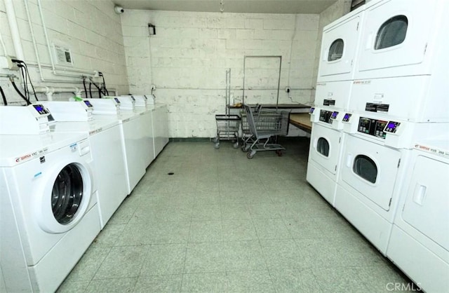 common laundry area with light floors, stacked washer and clothes dryer, concrete block wall, and washing machine and dryer