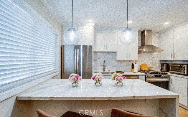 kitchen featuring decorative light fixtures, appliances with stainless steel finishes, white cabinets, a sink, and wall chimney exhaust hood