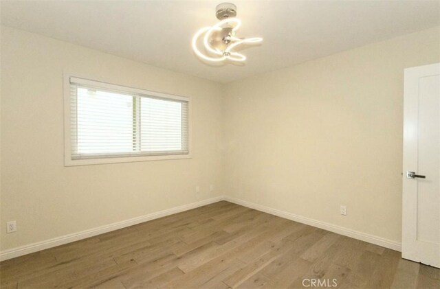 empty room featuring a chandelier, light wood-style flooring, and baseboards