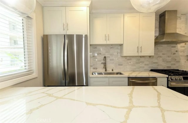 kitchen featuring decorative backsplash, a wealth of natural light, appliances with stainless steel finishes, a sink, and wall chimney exhaust hood