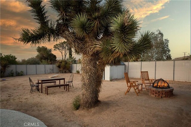 yard at dusk featuring an outdoor structure, a storage unit, a fire pit, and a fenced backyard