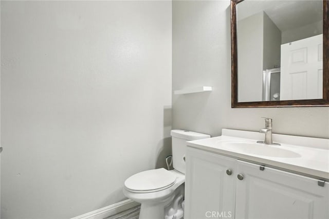 bathroom with toilet, an enclosed shower, vanity, and baseboards
