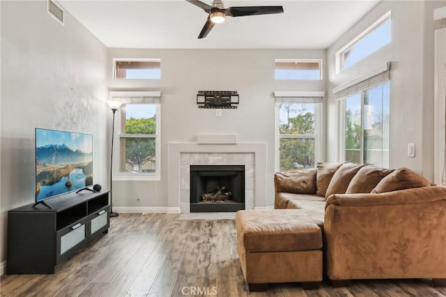 living area featuring a tile fireplace, wood finished floors, a ceiling fan, and visible vents