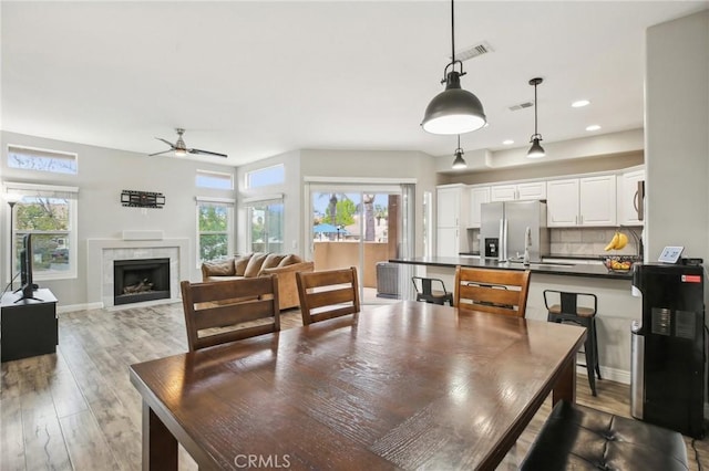 dining room featuring recessed lighting, light wood finished floors, a tile fireplace, a ceiling fan, and visible vents