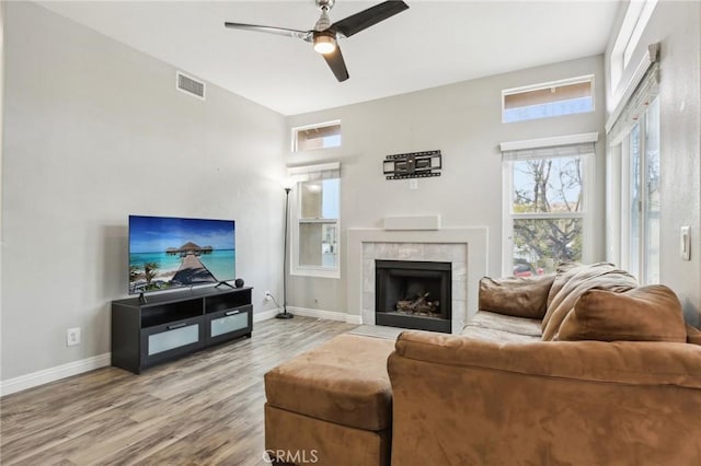 living area with visible vents, a tiled fireplace, wood finished floors, and baseboards