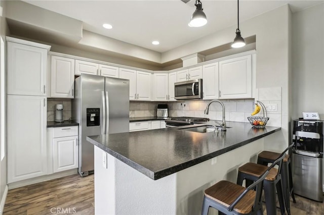 kitchen with a sink, a peninsula, appliances with stainless steel finishes, and wood finished floors