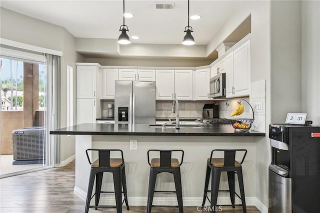 kitchen with a sink, stainless steel appliances, visible vents, a peninsula, and white cabinets
