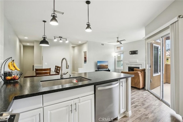 kitchen featuring a sink, a fireplace, white cabinetry, stainless steel dishwasher, and dark countertops