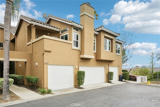 view of property with an attached garage, stucco siding, and a chimney