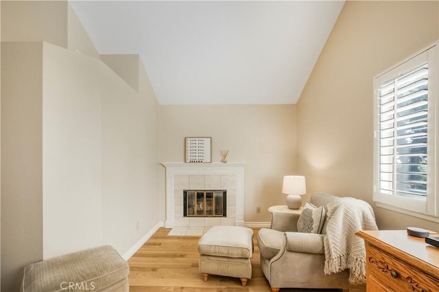 sitting room with a tile fireplace, baseboards, vaulted ceiling, and light wood-style floors