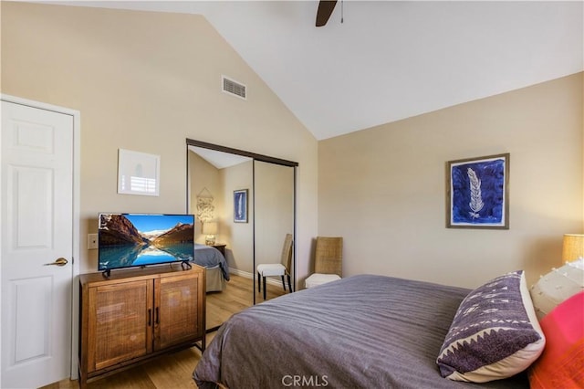 bedroom featuring a closet, high vaulted ceiling, a ceiling fan, visible vents, and wood finished floors