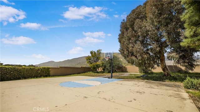 view of sport court featuring basketball hoop, fence, and a mountain view