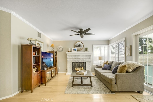 living room with crown molding, a ceiling fan, a brick fireplace, and light wood-type flooring