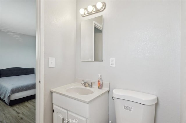 ensuite bathroom with toilet, wood finished floors, vanity, and ensuite bathroom