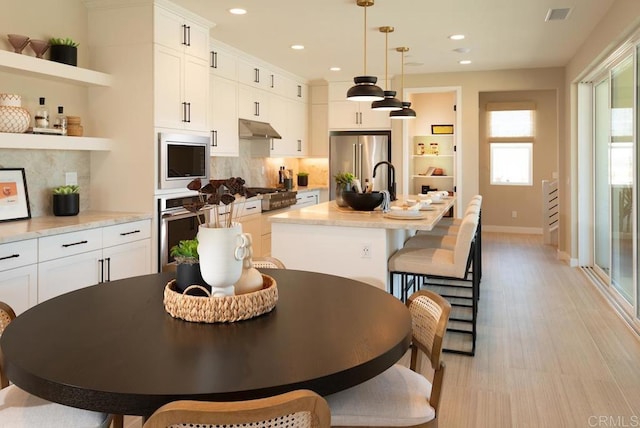 kitchen featuring under cabinet range hood, decorative backsplash, open shelves, visible vents, and appliances with stainless steel finishes