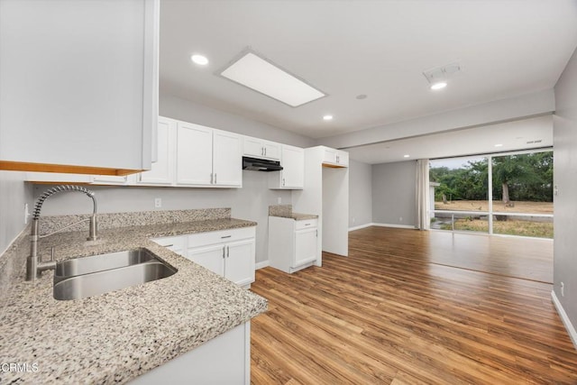kitchen featuring white cabinetry, a sink, under cabinet range hood, light stone countertops, and light wood finished floors