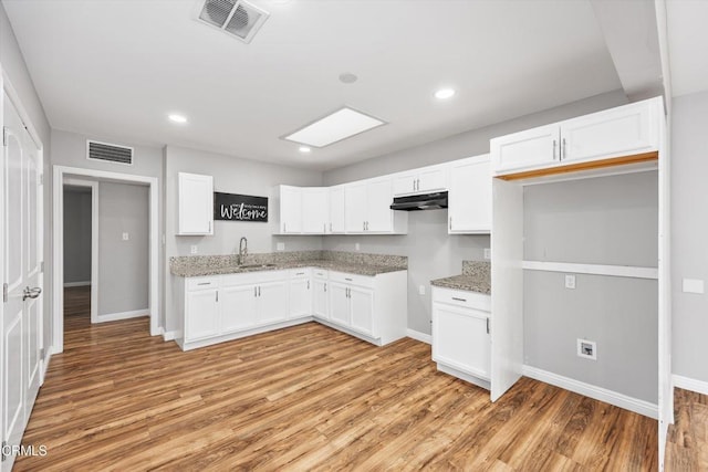 kitchen featuring a sink, baseboards, under cabinet range hood, and visible vents