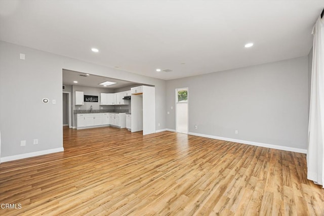 unfurnished living room with baseboards, recessed lighting, light wood-style floors, and a sink