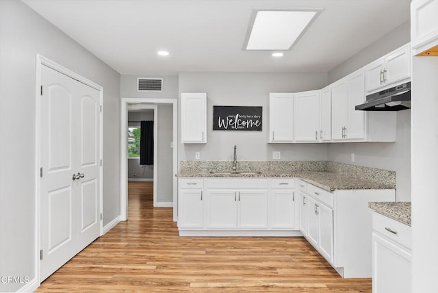 kitchen featuring a sink, under cabinet range hood, light stone countertops, light wood finished floors, and recessed lighting