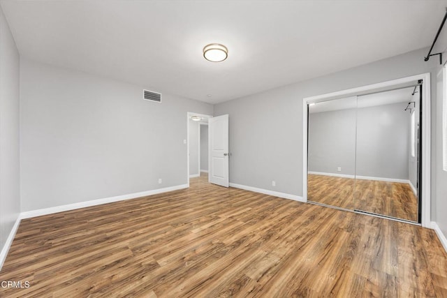 unfurnished bedroom with baseboards, visible vents, wood finished floors, and a closet