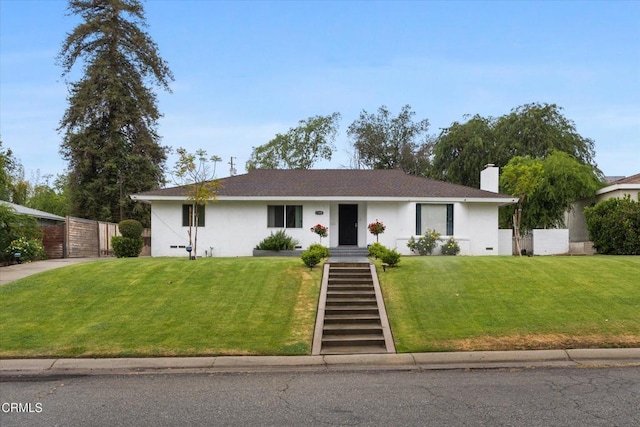 ranch-style home featuring a front lawn, a shingled roof, a chimney, stucco siding, and fence