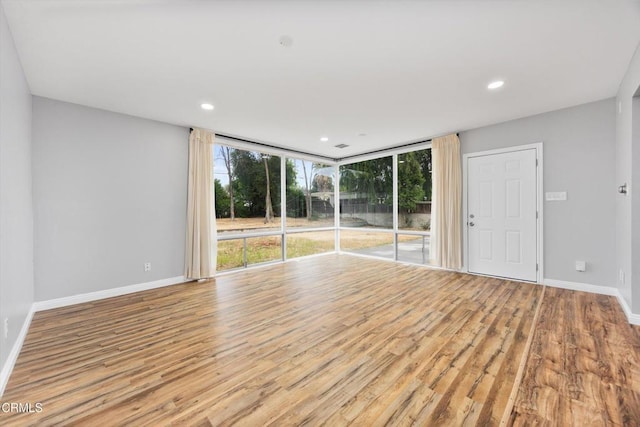 empty room featuring a wall of windows, wood finished floors, recessed lighting, and baseboards